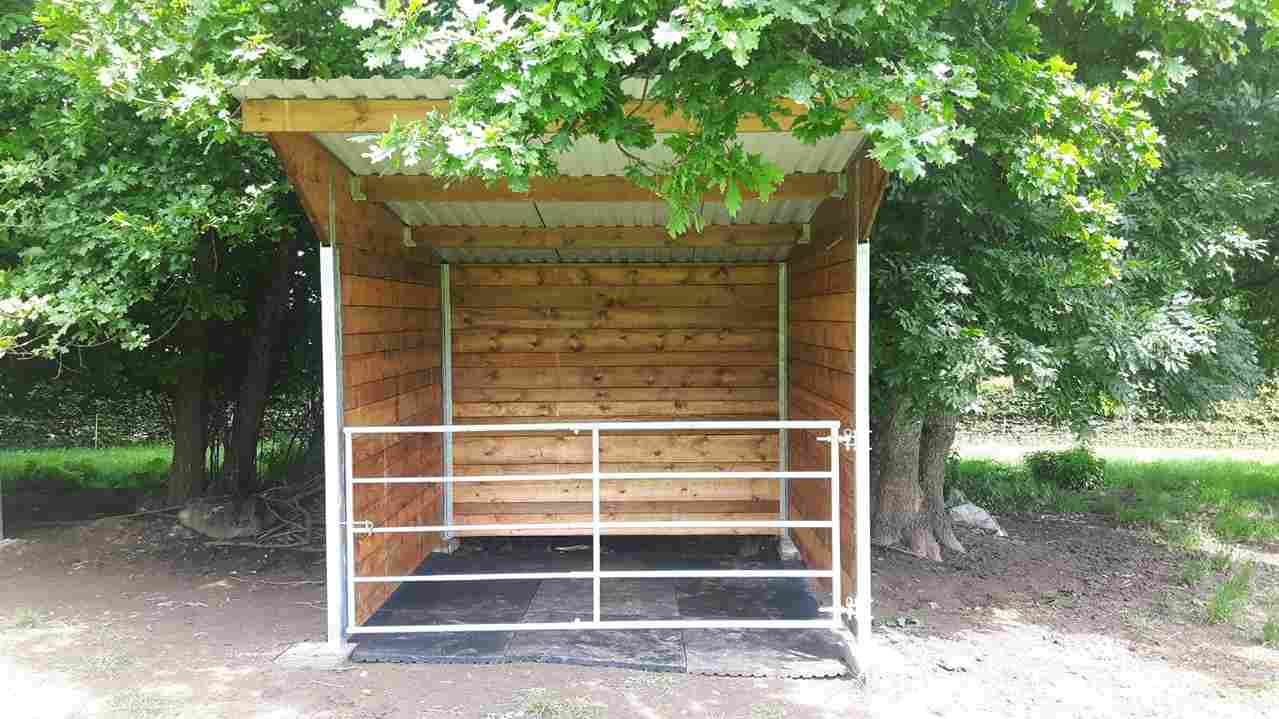 Abri pour chevaux en bois à ossature métallique, vue de près et de face, avec une barrière en acier.